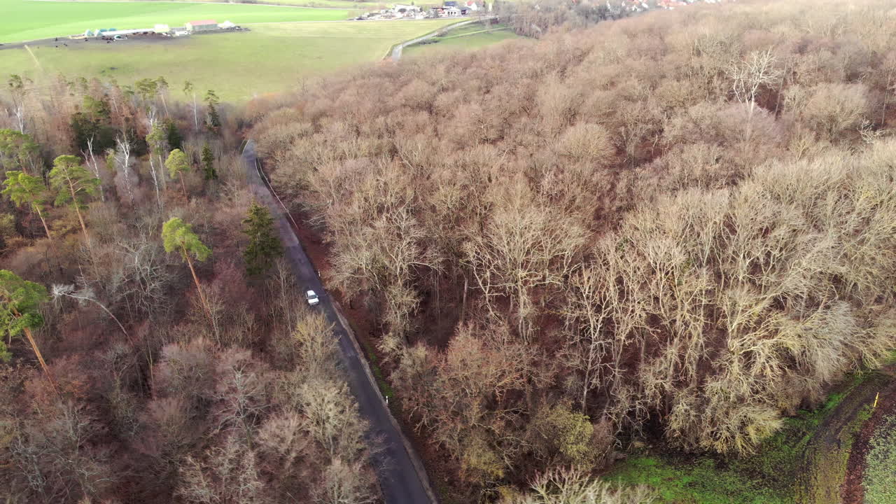 겨울 동안 빈 도로에서 숲을 통해 운전하는 흰색 자동차의 공중