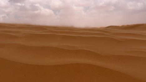 sand blowing over desert dunes surface on windy and cloudy day in tunisia