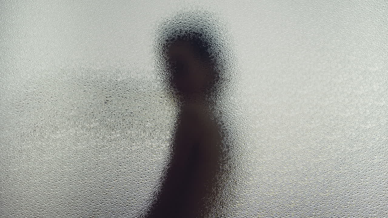 A female silhouette behind the frosted glass moves slowly