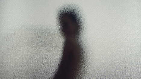 a female silhouette behind the frosted glass moves slowly