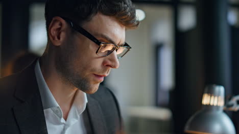 Closeup-late-manager-working-office-in-lamp-light.-Serious-man-trading-broker