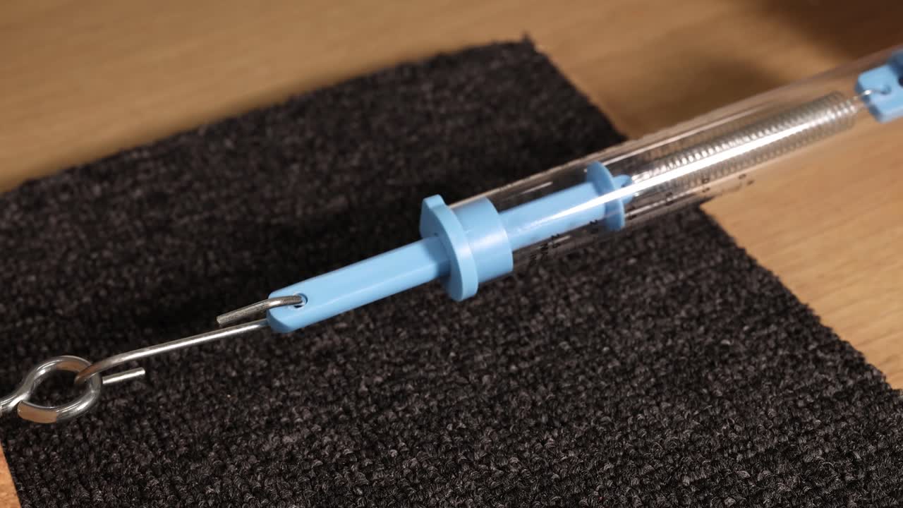 A spring scale measures friction as a wooden block is dragged across a carpeted surface. Close-up, well-lit, macro view