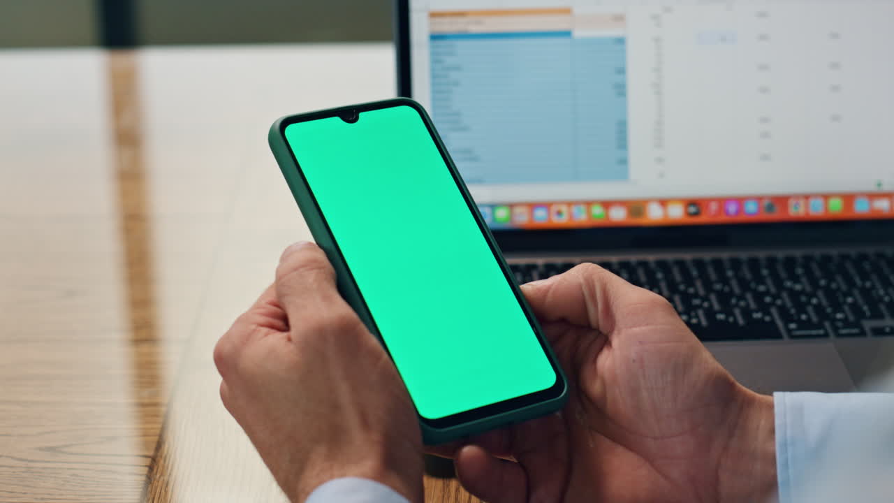 las manos del empleado sosteniendo el teléfono de pantalla verde en la oficina de primer plano. hombre usando el teléfono