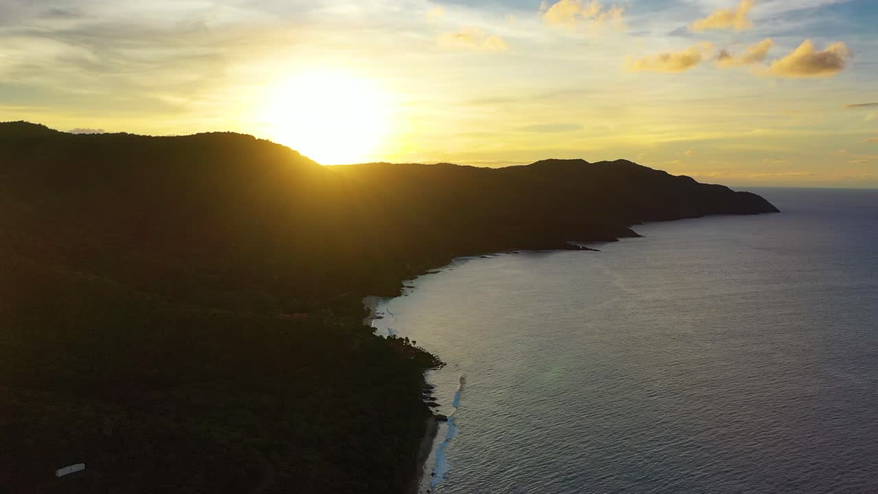 Serene sunset aerial footage of a forested peninsula in St. Croix, where shadows stretch over calm Caribbean waters and the glowing sky creates a vivid island silhouette