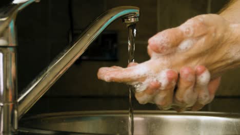 washing hands and rinsing off the soap with water in a home kitchen sink slow motion