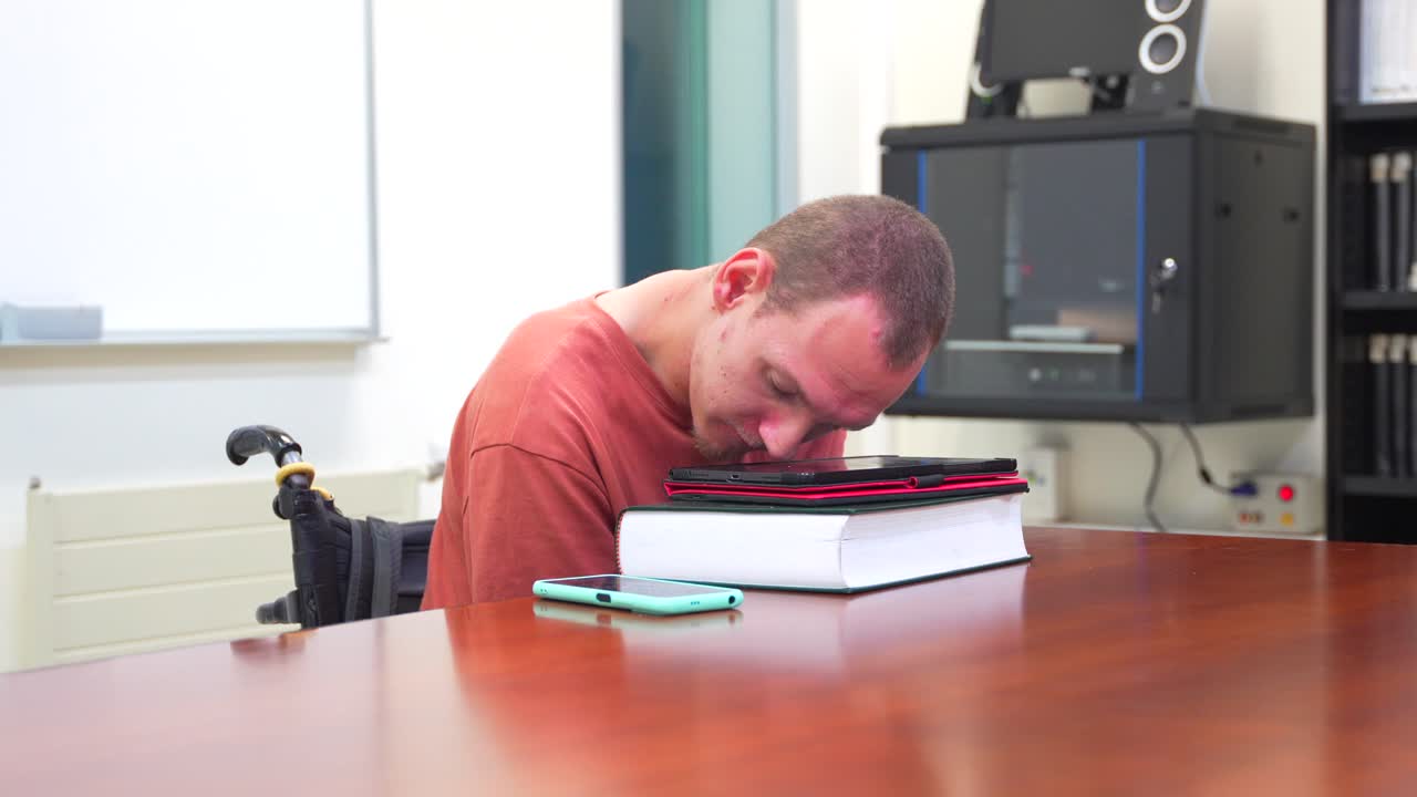 Man sitting in wheelchair at a table with books and electronics