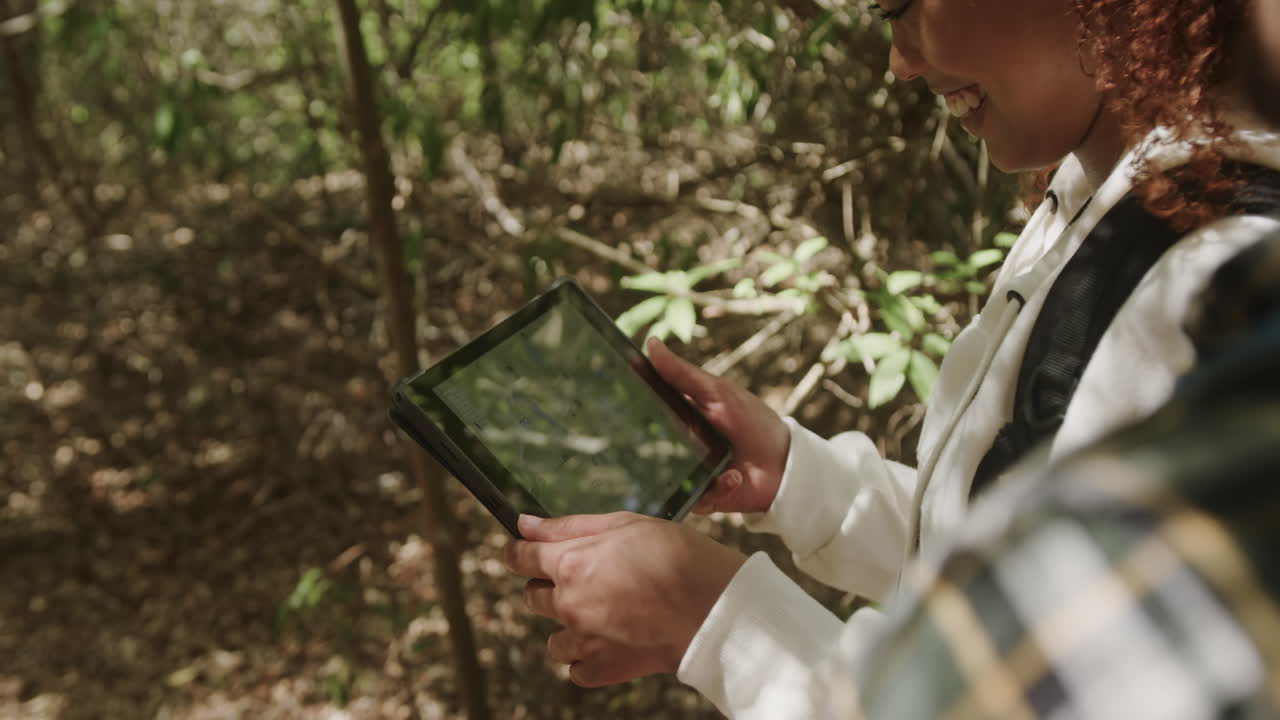 feliz pareja afroamericana con mochila, usando tableta en el bosque, cámara lenta