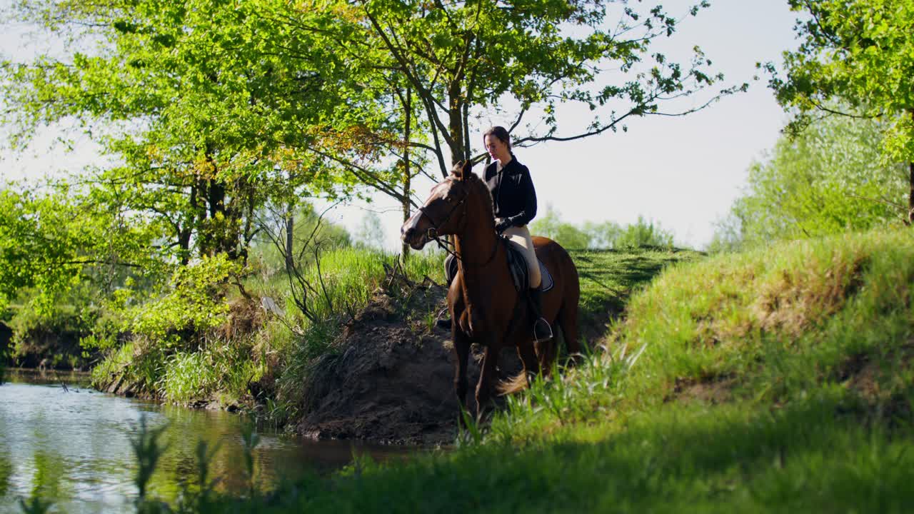 Woman horseback riding near a river in a lush green forest