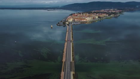 意大利托斯卡尼 (tuscany) 蒙特阿根廷里奥 (monte argentario) 和马雷玛公园 (maremma park) 附近的岛屿城市奥贝特洛 (orbetello) 的公路上,有蓝色的天空和平静的蓝色水