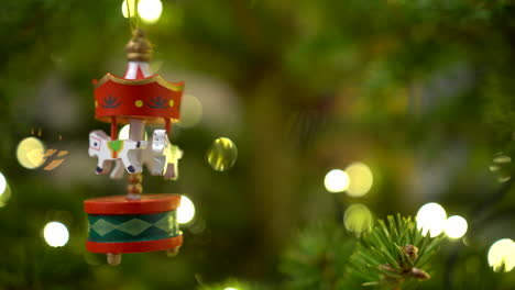 rotating wooden carousel with white horses as hristmas tree decor hanging on the fir tree with blurred lights in the background in december