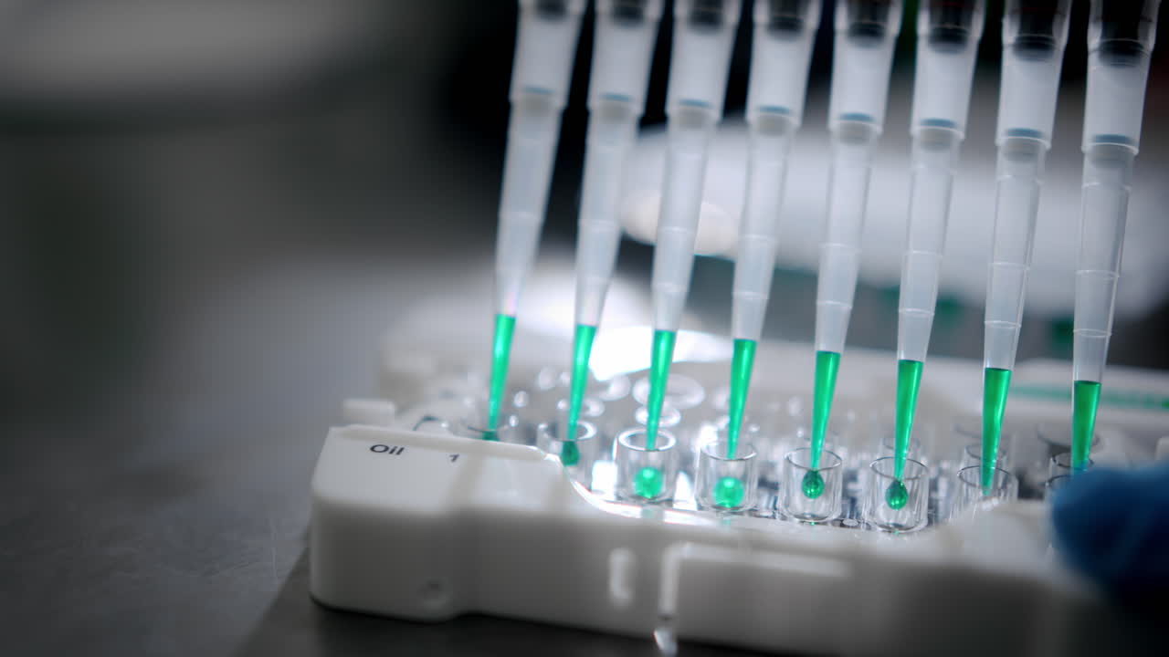 Multiple pipette tips inserting green liquid into test tubes