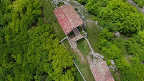 toma aérea de drones captura una ermita de piedra con un techo rojo escondido entre el exuberante follaje verde del bosque en la cima del monte erga