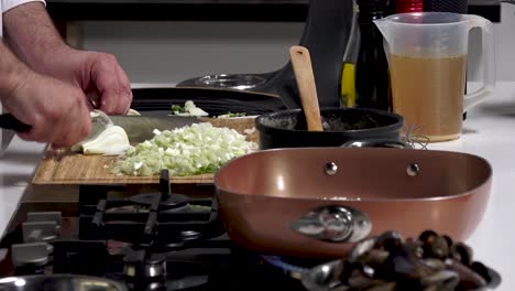 skilled cook chops vegetables and prepares ingredients for a seafood pasta dish in a contemporary kitchen. fresh clams, onions, and olive oil create a flavorful experience