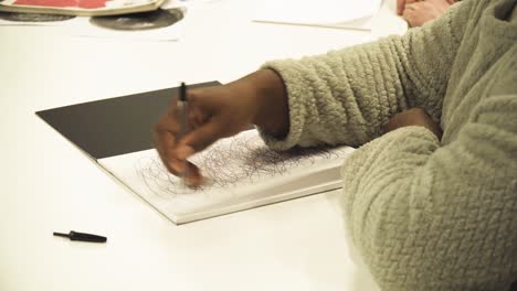 african woman close up hand drawing random circle patterns on paper practicing learning patterns in arts school wearing cosy warm jumper moving hand without stopping