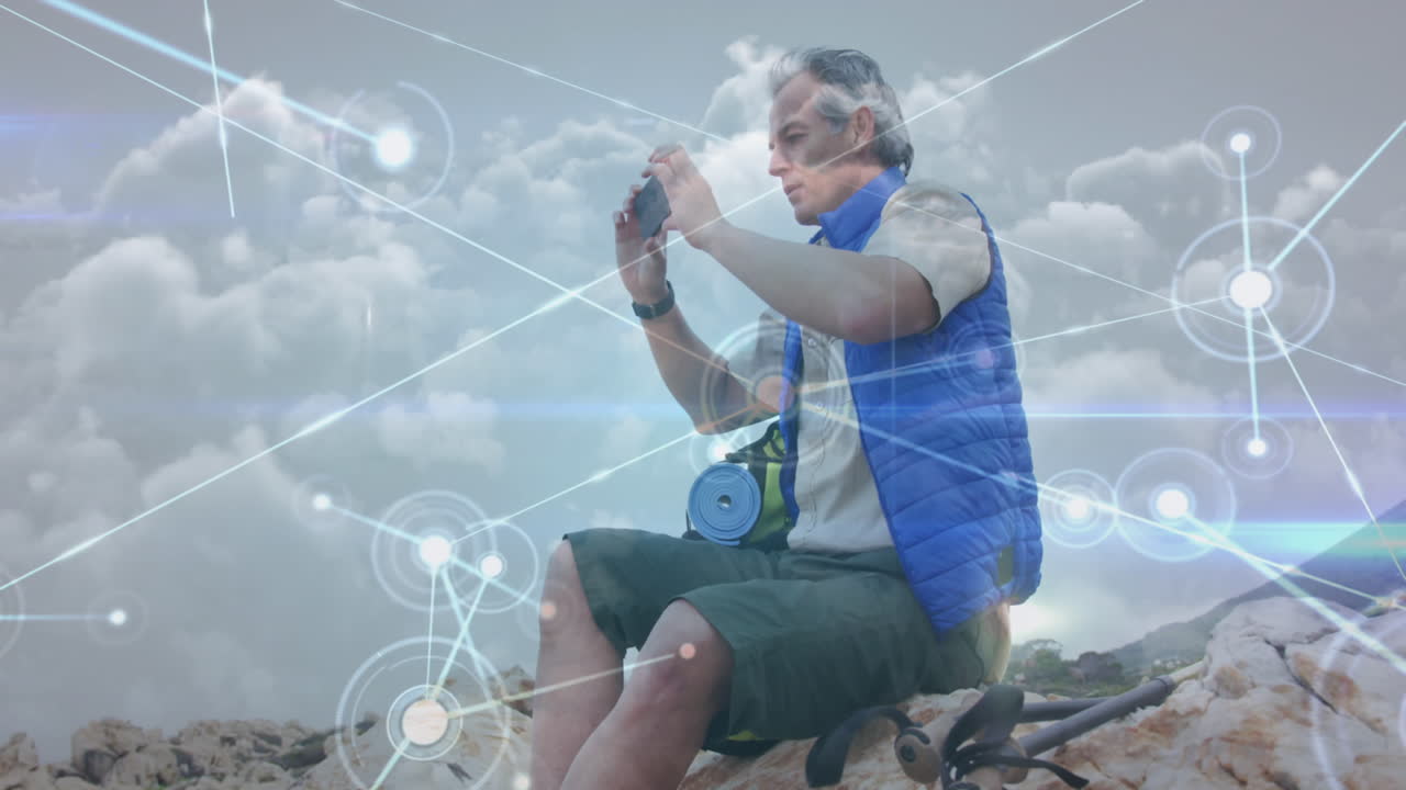 hombre caucásico mayor sentado en la ladera tomando una foto con un teléfono inteligente, a través de una red de conexiones