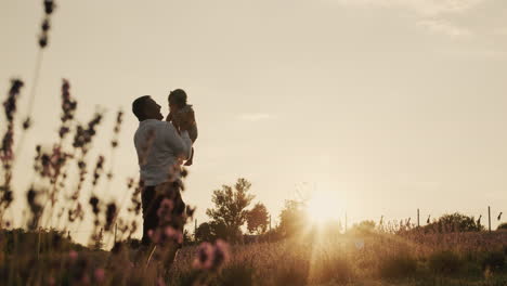 Ein-Aktiver-Vater-Wirft-Seine-Tochter-Bei-Sonnenuntergang-Aus.-Spielen-Mit-Einem-Kind-In-Einem-Lavendelfeld