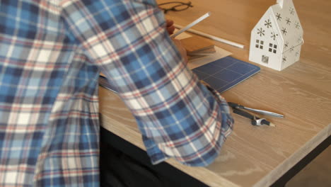 ingeniero dibujando planos en una mesa de madera con lápiz, vista trasera de cerca