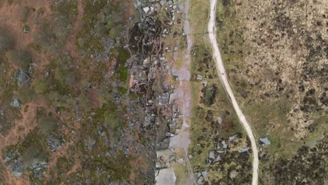 Aerial,-birds-eye-footage-of-a-stunning-rock-formation-and-long-rural-trail-through-open-moorland