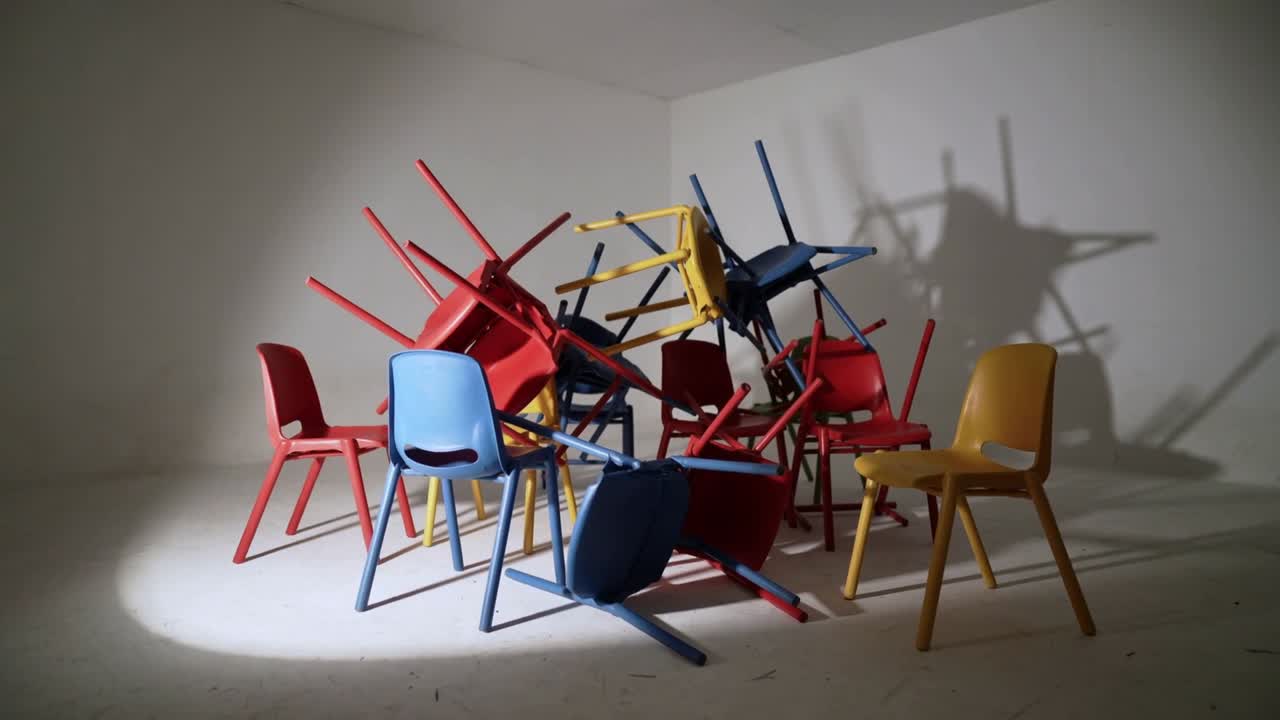 Un spot lumineux mobile effleure des chaises en plastique qui se stabilisent et s'inclinent dans un studio blanc, projetant une ombre nette.