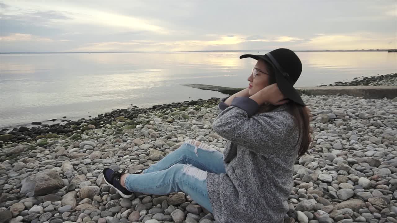 mujer sentada en una playa de guijarros al atardecer