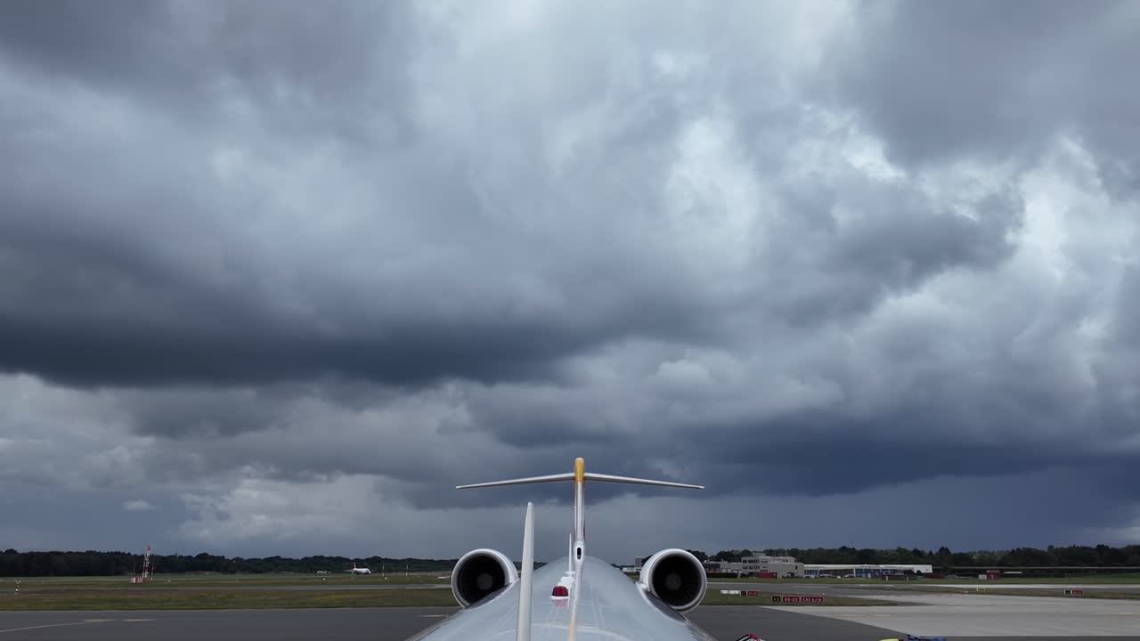 A rear view from the top of the fuselage of a white color fuselage jet at the parking stand, under a threatening stormy sky