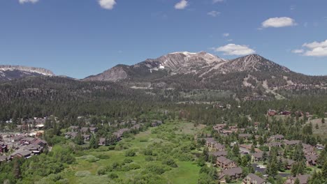 4k drone footage slow pan right of beautiful mammoth mountain in the summertime with a view of a lush green meadow and cabins