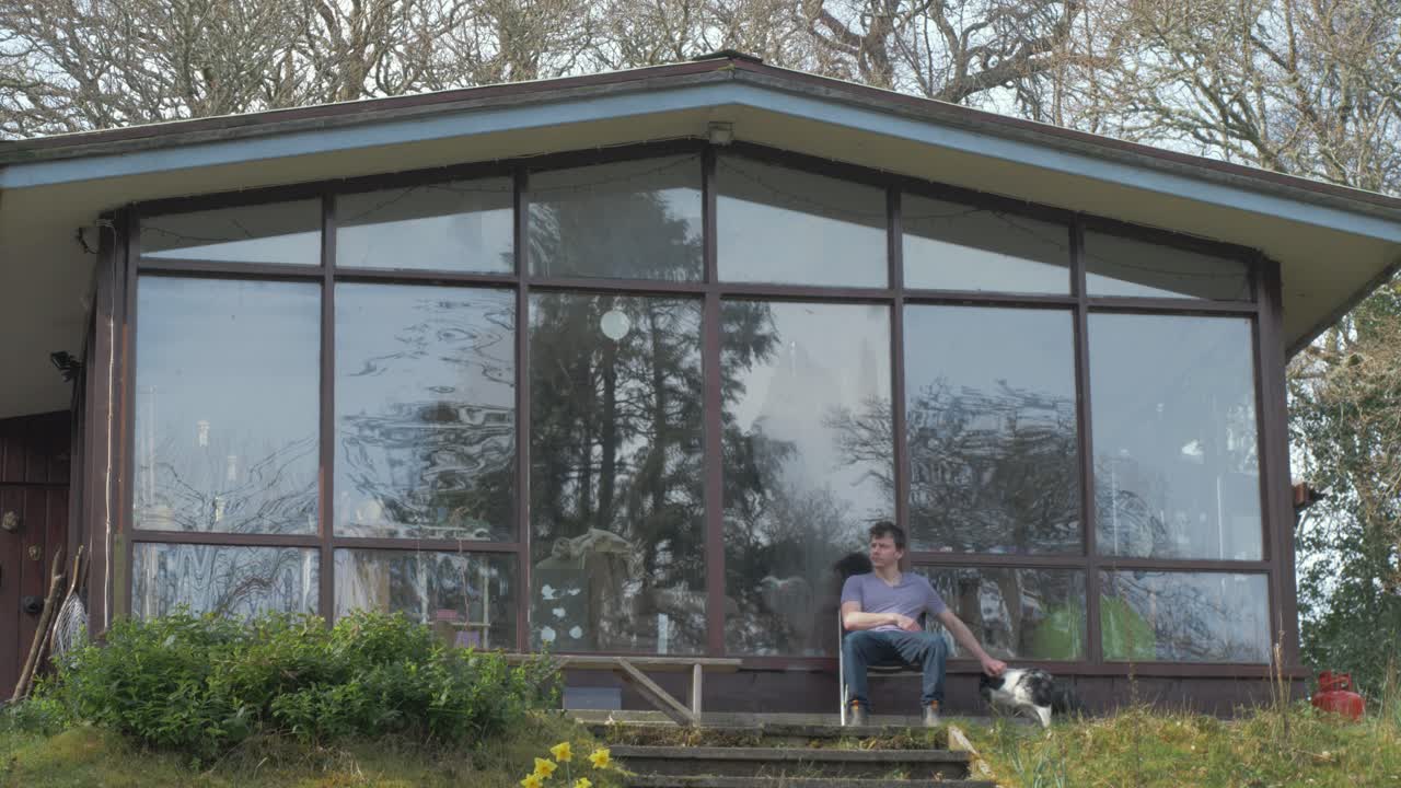 Young man relaxing in front of cabin in woods with his dog
