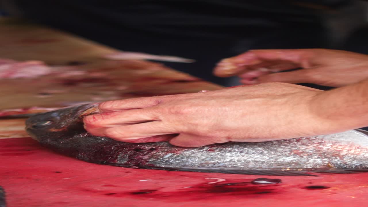 한 남자 가 테이블 위 에 있는 물고기 를 청소 하고 있다