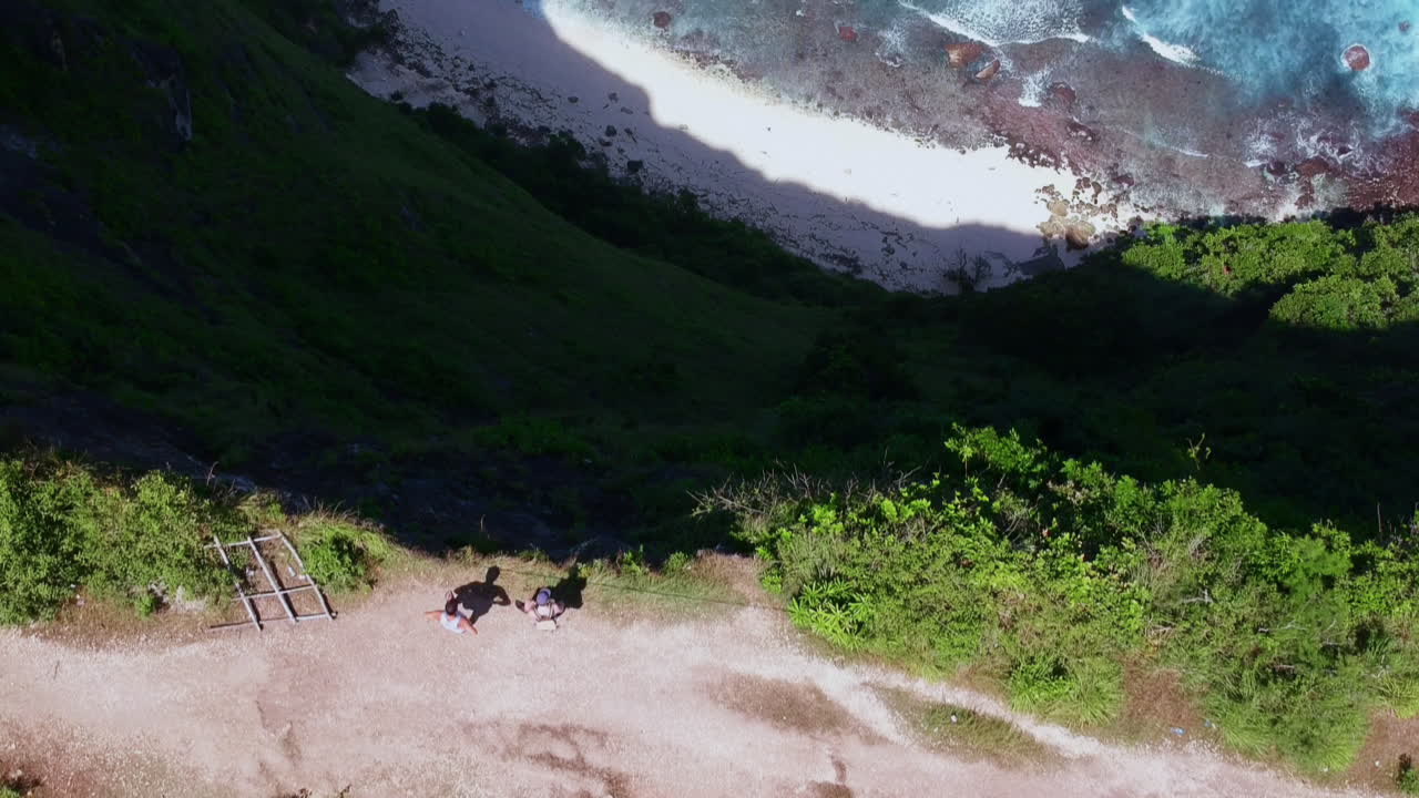 la cámara vuela sobre dos personas y revela un acantilado muy profundo con el mar