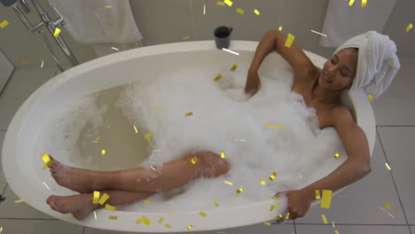 animation of gold confetti falling over happy african american woman lying in bathtub