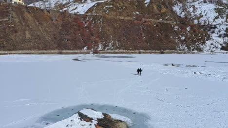 couple holding hands while walking in the frozen and snow-covered lake at winter in sissu, himachal pradesh, india