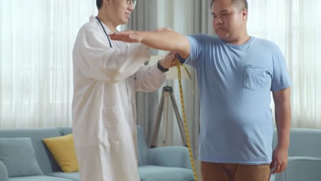 클리닉에서 한 남성 환자를 가진 아시아 남성 의사. 환자는 무게를 측정하는 기계를 사용하고, 의사는 환자의 팔을 측정하는 테이프를 사용합니다.