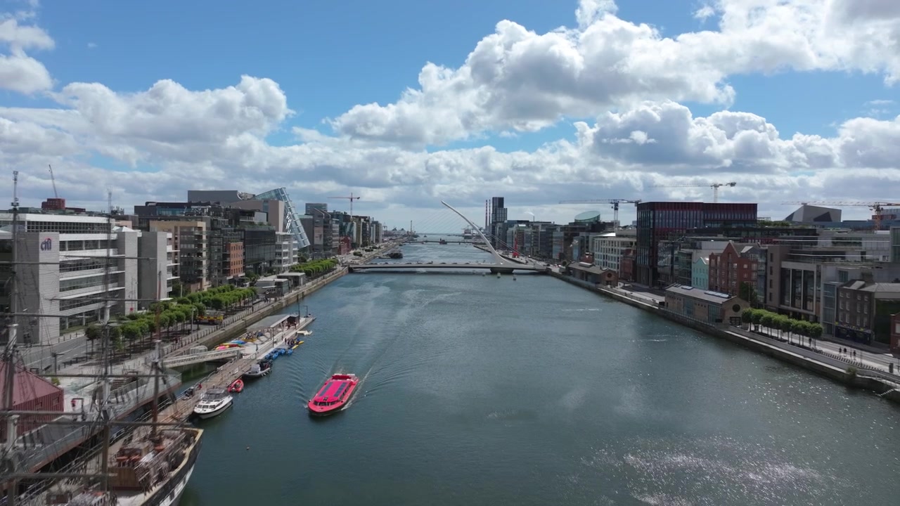 Kamera liukuu Dublinin June26-rantakadun varrella, kun punainen turistivene liikkuu kanavaa pitkin modernien toimistorakennusten alla.