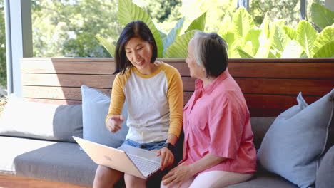showing laptop, young asian woman helping senior asian woman with technology on sofa