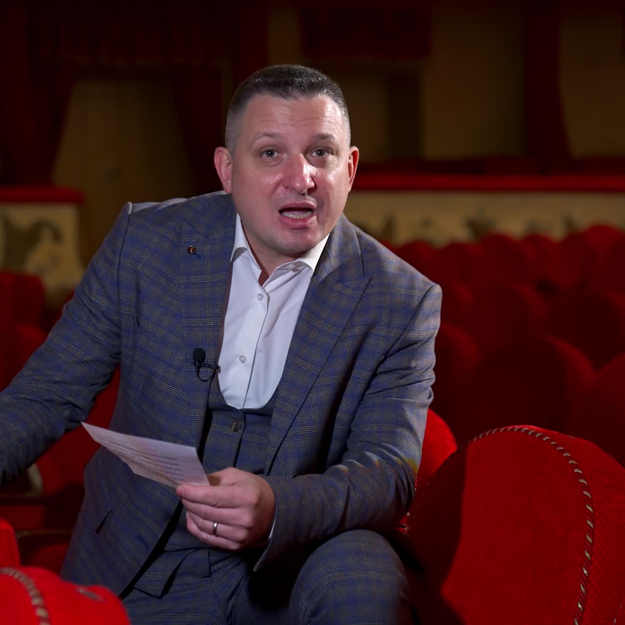 Actor at rehearsal in auditorium. Man repeating monologue while sitting among red chairs in the empty hall. Speaker rehearsing before the performance