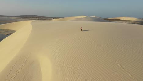 drone shot of a bike cruising through sand dunes during sunset