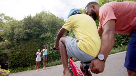 Padre-Afroamericano-Enseñando-A-Su-Hijo-A-Andar-En-Bicicleta,-Madre-Y-Hermana-Aplaudiendo,-Cámara-Lenta