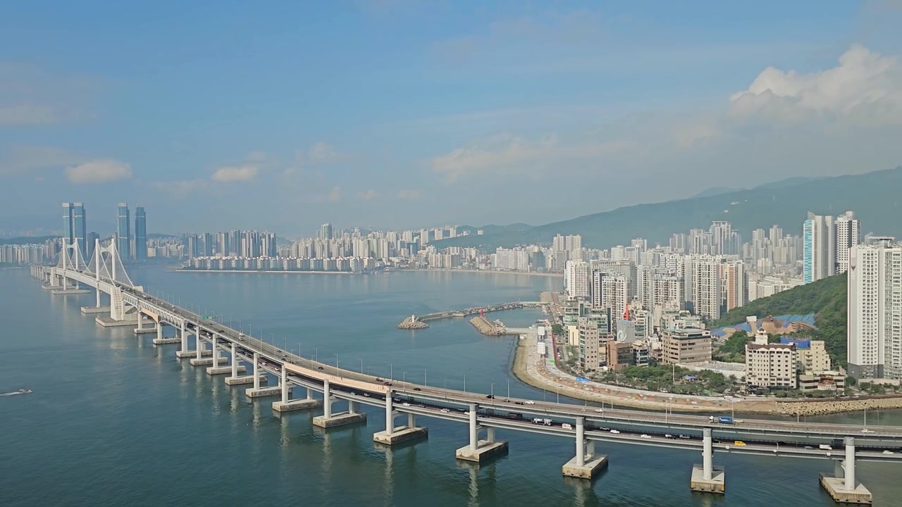Auto che attraversano il ponte Gwangan sul mare con lo skyline di Busan e gli edifici della città, Corea del Sud - ripresa aerea con zoom indietro.