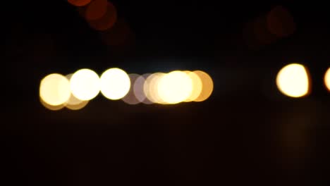 Steady-stream-of-car-headlights-out-of-focus-traveling-toward-the-viewer,-bokeh-balls,-blurred-lights,-dark-tunnel
