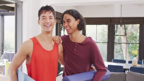 Retrato-De-Una-Feliz-Pareja-Masculina-Diversa-Sosteniendo-Colchonetas-De-Yoga-En-La-Sala-De-Estar