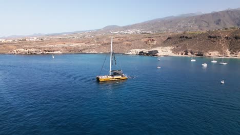 people-bathing,-catamaran-in-blue-sea-water,-beautiful-bay-on-an-island,-tenerife,-boat,-summer,-drone