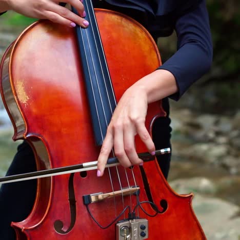 woman plays the cello outdoors. female musician playing the instrument on natural river background in summer. musical equipment in womans' hands.