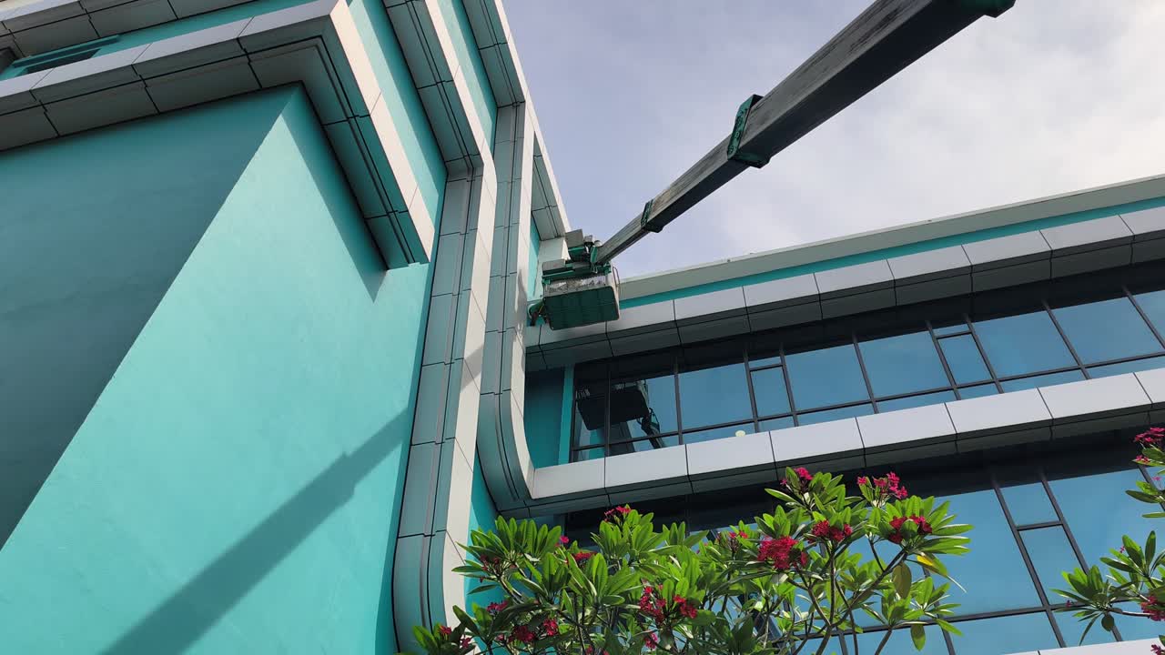Uma plataforma elevatória realiza manutenção e limpeza de fachadas de arranha-céus. Os trabalhadores usam EPI completo enquanto posicionados com segurança na cesta elevatória. Protocolos de segurança são rigorosamente seguidos nesta altura