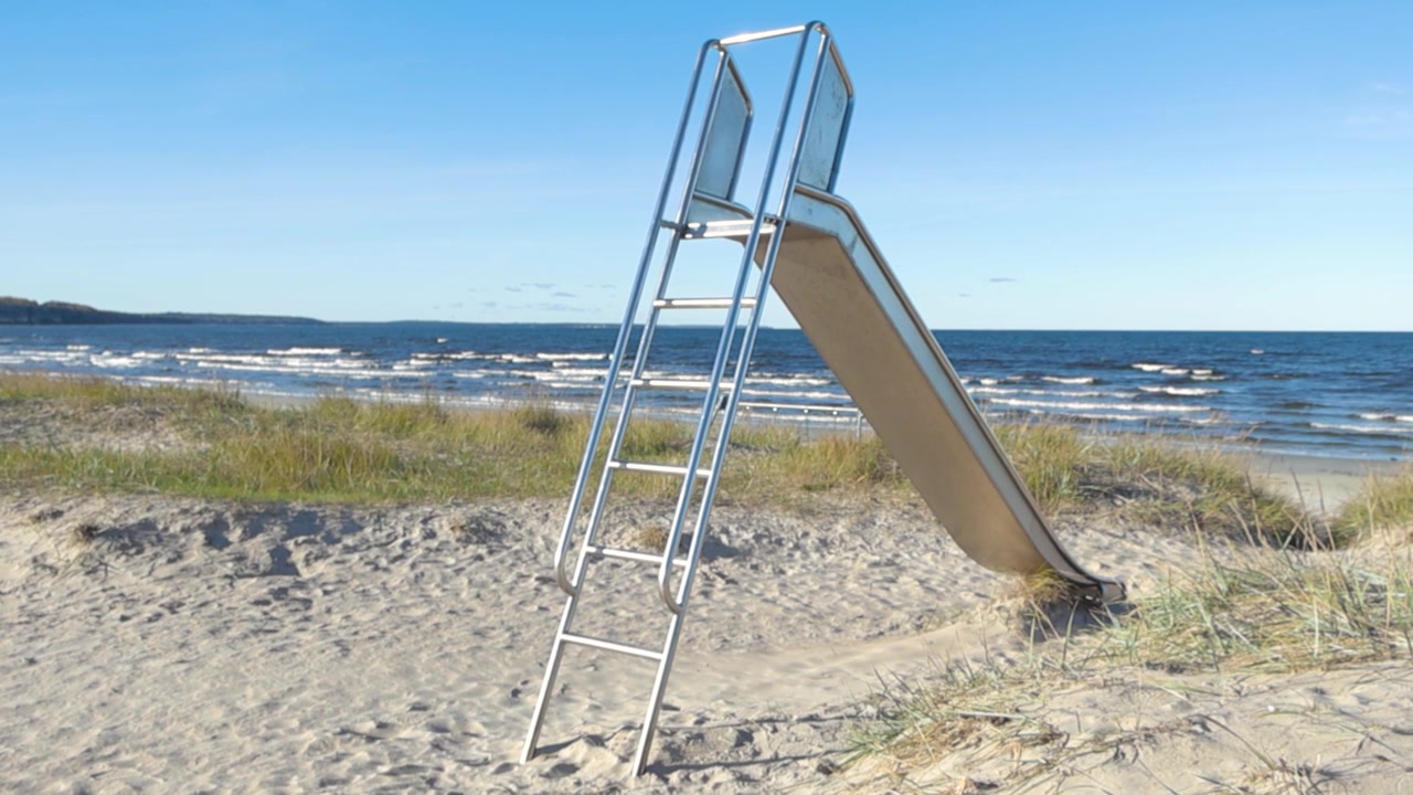Riprese panoramiche di uno scivolo in acciaio inossidabile su una spiaggia deserta a Vääna Jõesuu, Estonia. Spiaggia sabbiosa costiera con erba, scivolo metallico e vista del mare blu con onde spumeggianti durante una giornata di sole