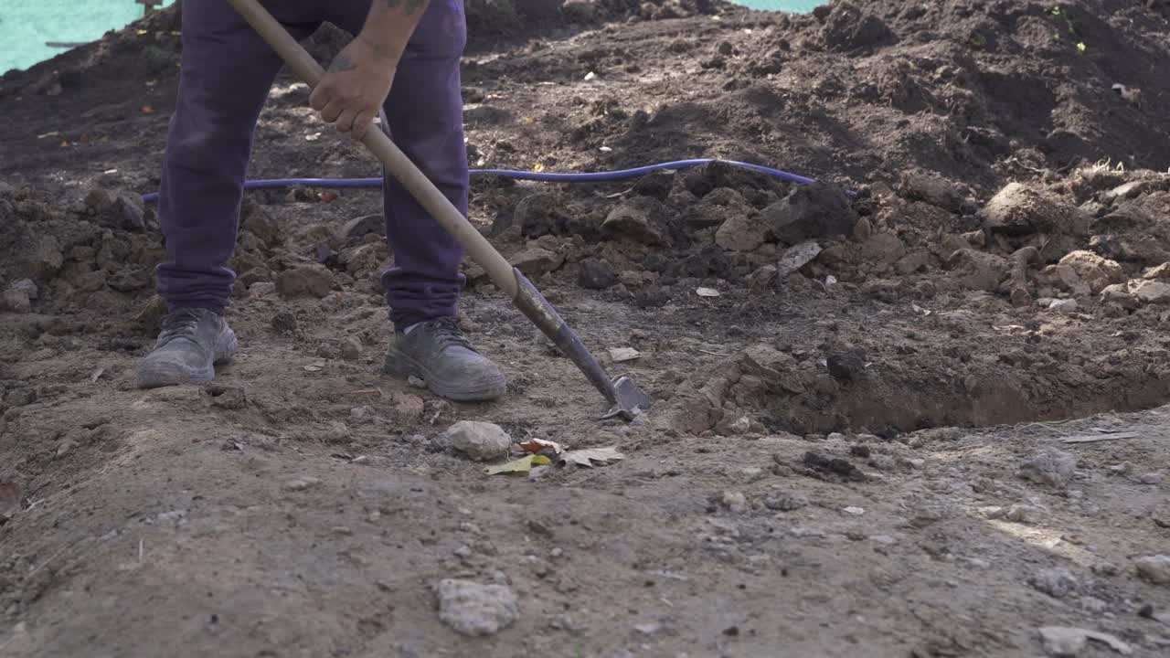 cierra el ángulo bajo del hombre de trabajo con una pala cavando un hoyo afuera en el sitio de construcción - 4k