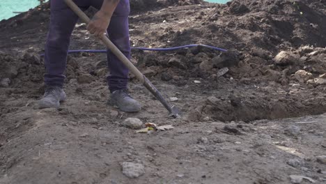 Cierra-El-ángulo-Bajo-Del-Hombre-De-Trabajo-Con-Una-Pala-Cavando-Un-Hoyo-Afuera-En-El-Sitio-De-Construcción---4k