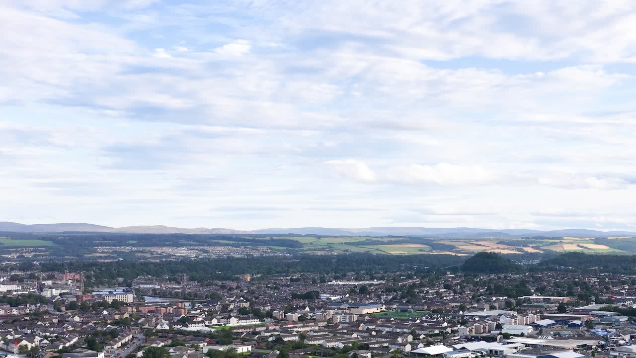 Drone camera slowly pans across Dundee rooftops, revealing suburban landscape and distant Scottish Highlands