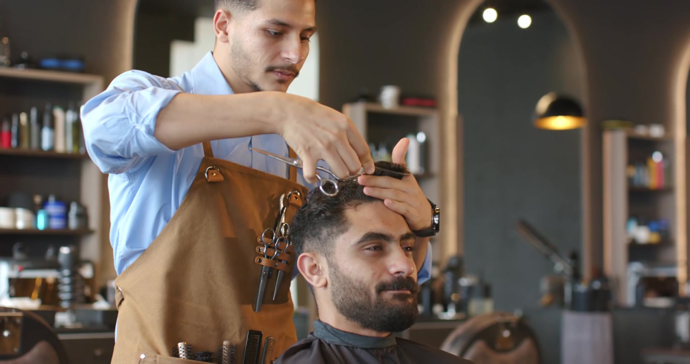 Afroamerikansk frisør og kunde i salonen, frisør i forklæde, klipper tophår med kam og saks