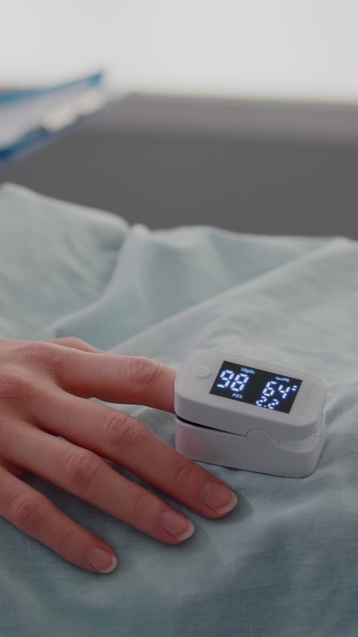 Vertical video: Close up of hospitalized woman with finger heart rate monitor showing pulse