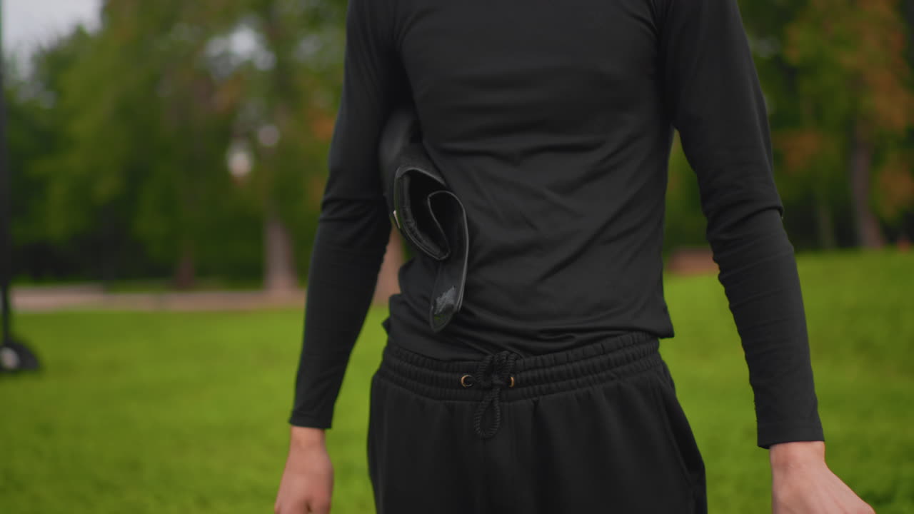 Athlet bereitet sich selbstbewusst vor, Boxer bereitet sich auf die Trainingseinheit vor, fokussierter Kämpfer passt die Ausrüstung in einem ruhigen Park an, Boxer sichert sorgfältig die Handschuhe und bereitet sich auf den Sparringskampf im Freien vor
